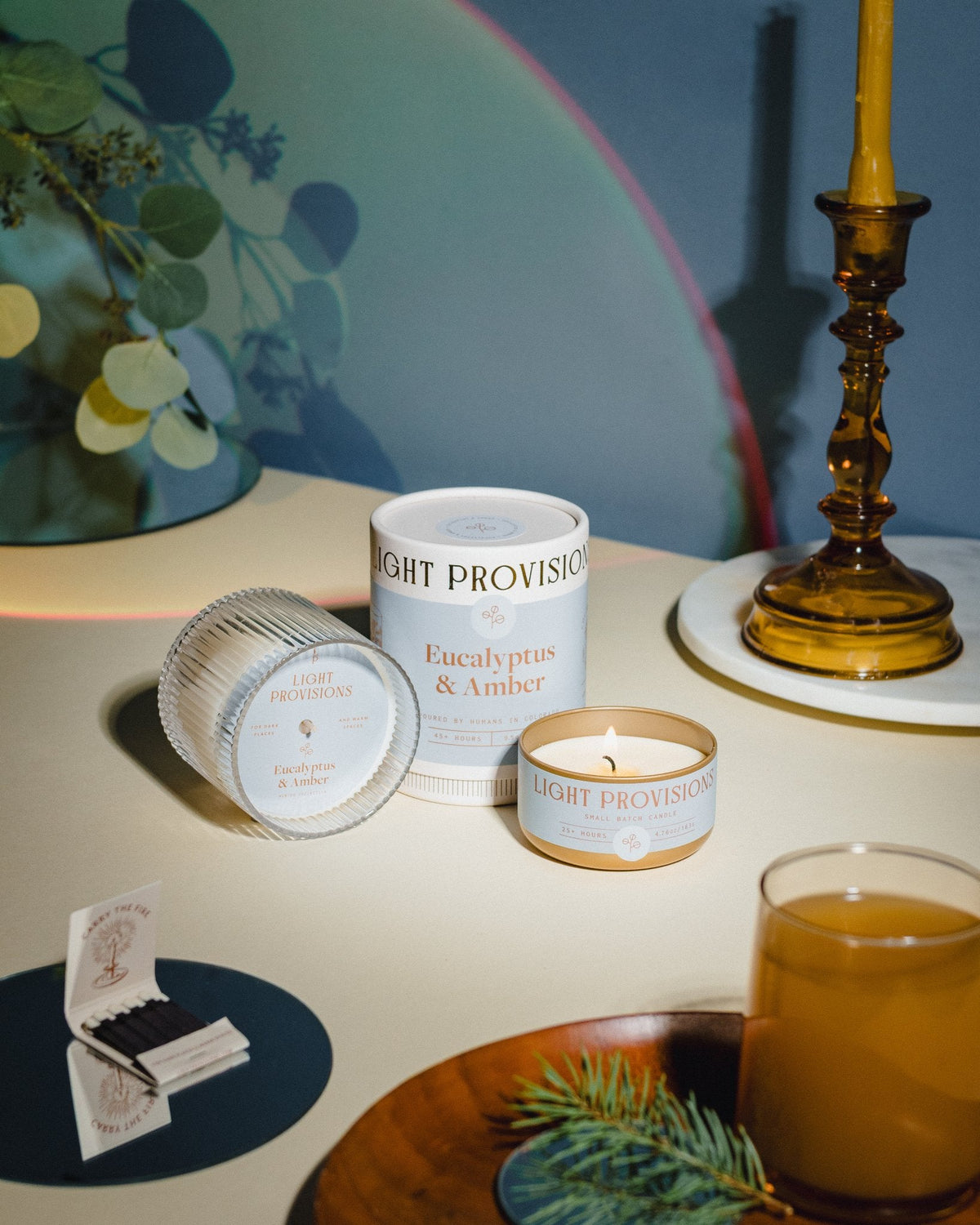 Eucalyptus & Amber candle and packaging beside cocktail, matches, and beeswax taper