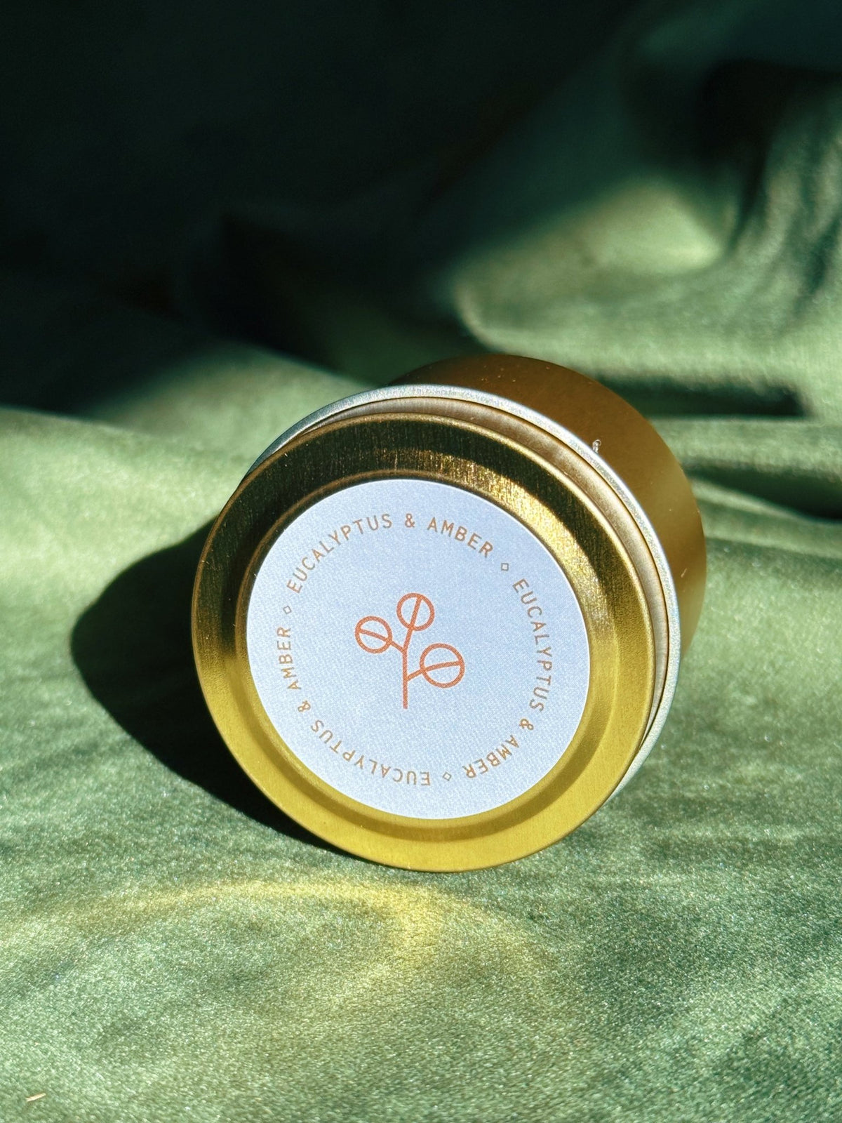 Gold sample tin labeled Eucalyptus and Amber photographed on green fabric with bright natural light.