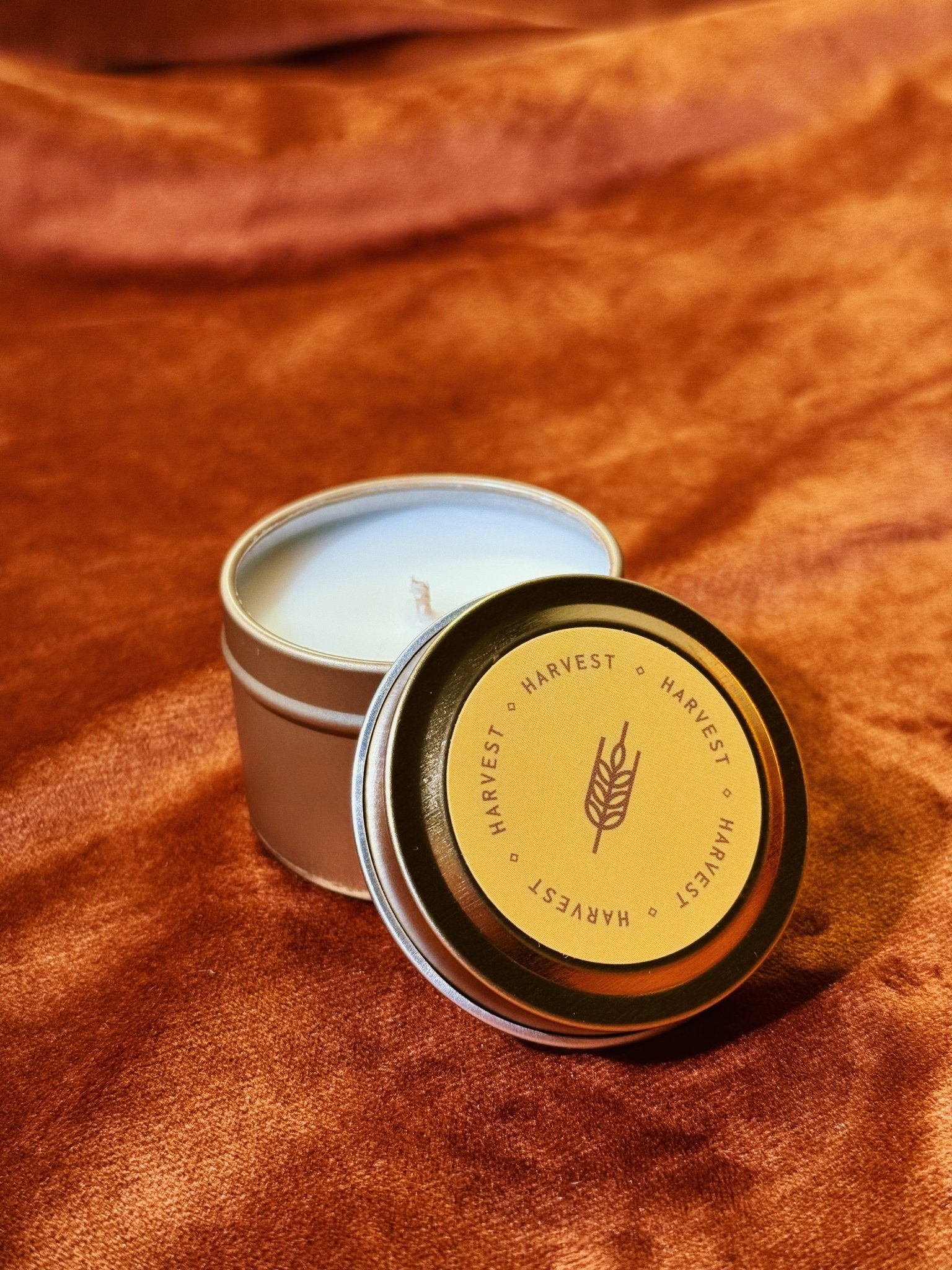 Harvest 2 oz tin sample candle with golden yellow lid on burnt orange fabric background