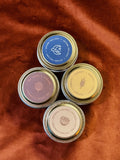 Four 2 oz tin sample candles — Autumn Twilight, Dry Leaves Cardamom, Harvest, Patchouli Nutmeg — on burnt orange fabric
