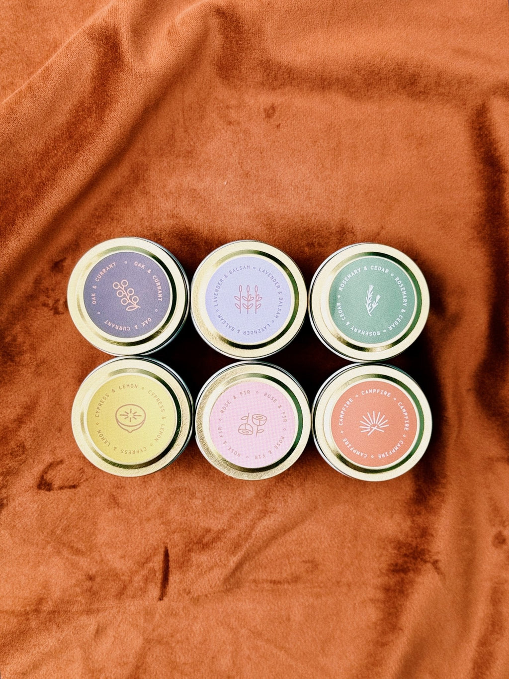 Six small flagship sample candles with lids on a brown fabric background