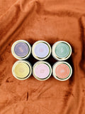Six small flagship sample candles with lids on a brown fabric background