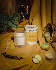 Light Provisions Harvest candle in signature glass tumbler and travel tin with fresh apples on mustard backdrop
