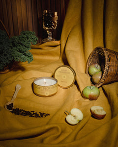 Light Provisions Harvest candle travel tin with lid off on mustard fabric with apples and greenery