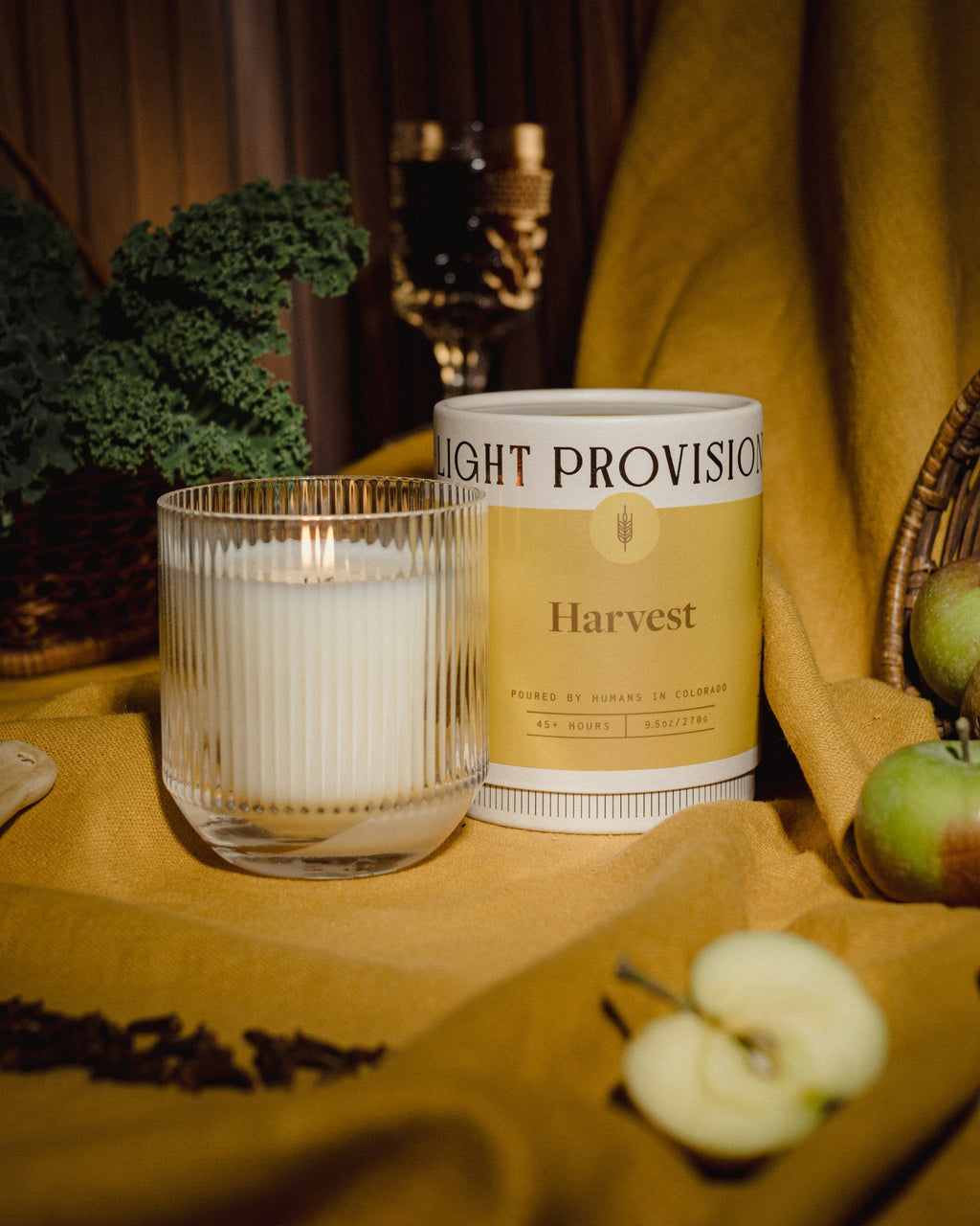 Harvest candle signature glass tumbler with Light Provisions dust cover and sliced apples on mustard backdrop