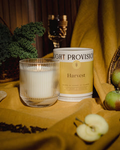 Harvest candle signature glass tumbler with Light Provisions dust cover and sliced apples on mustard backdrop