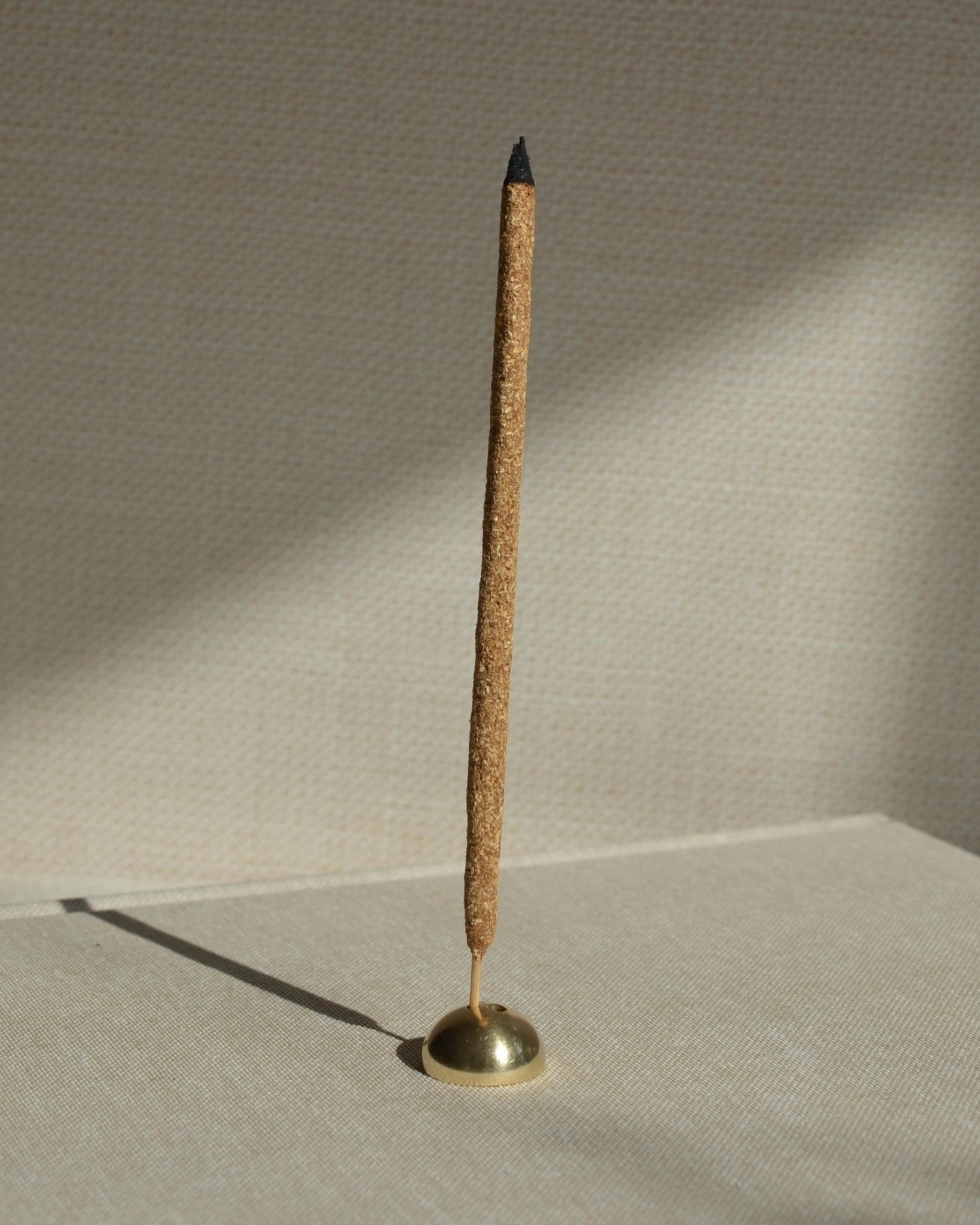Brass hemisphere incense holder holding a bamboo core incense stick, photographed in soft natural light.