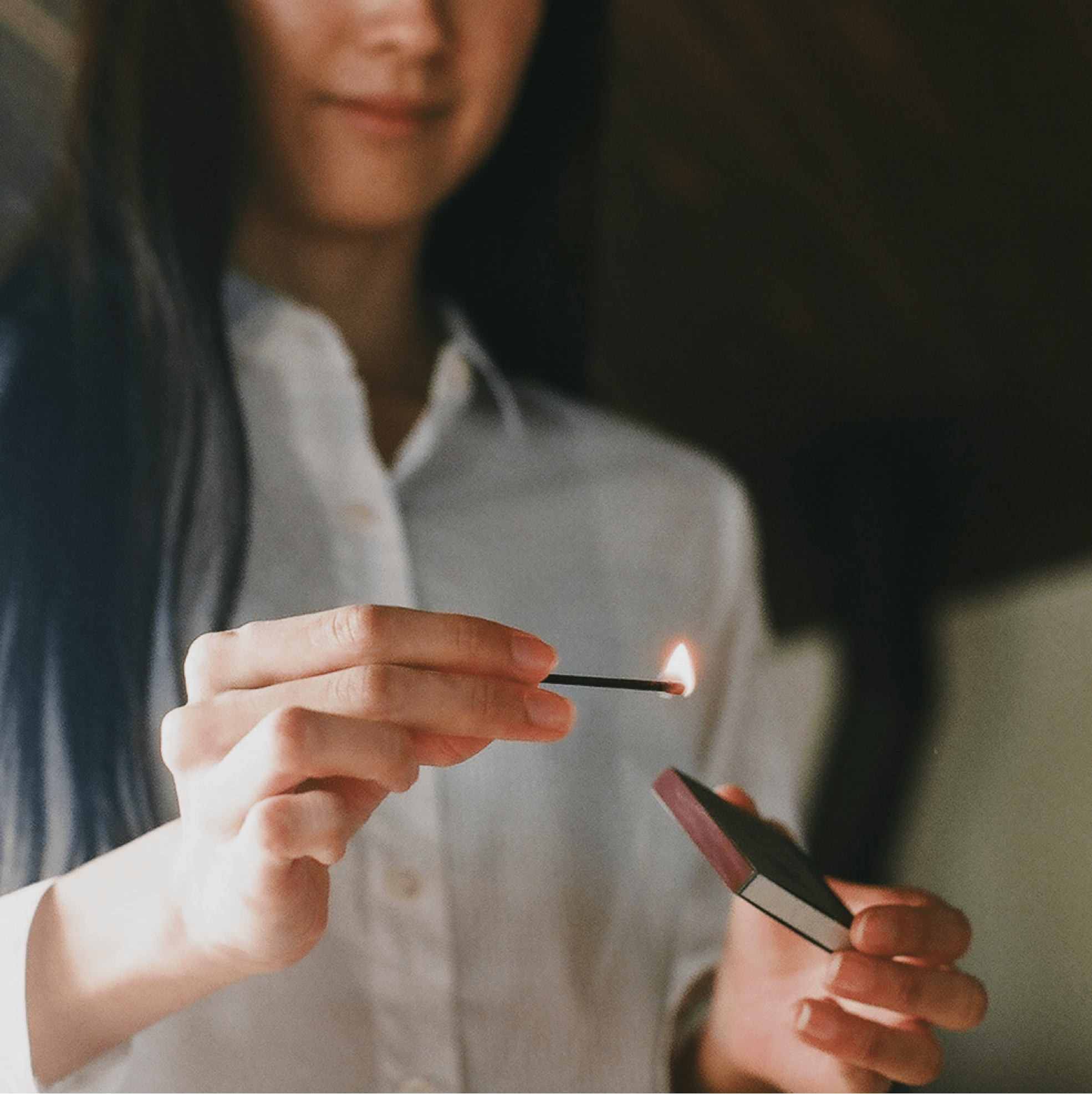 Person lighting a hibi incense match with the striking side of match box, blurred background