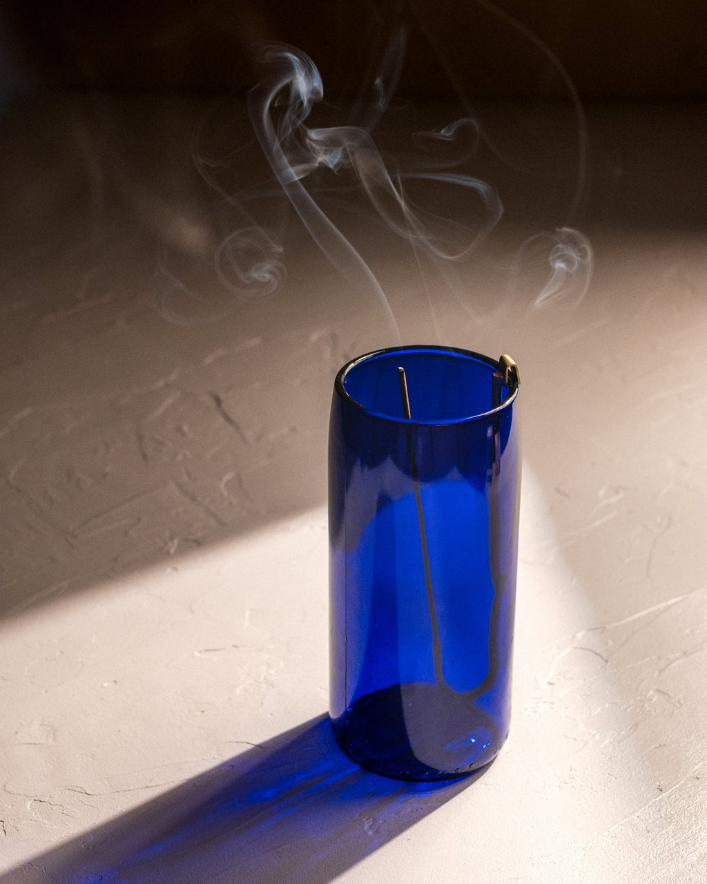 Brass hook incense holder hanging inside cobalt blue recycled bottle vase with burning incense