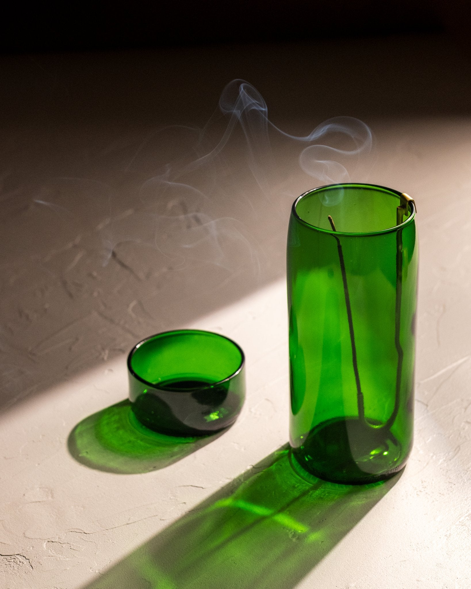 Brass hook incense holder hanging inside green recycled bottle vase with burning incense