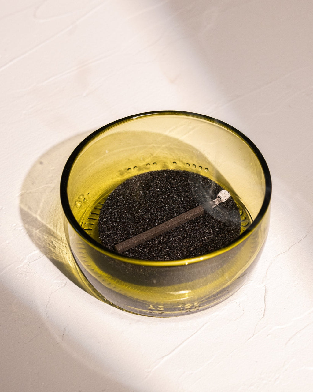 Lit HIBI incense match burning in recycled olive colored wine bottle glass incense dish