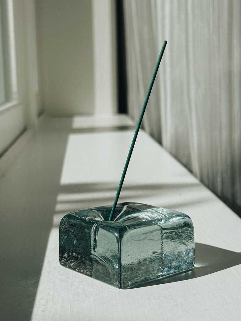 IYE recycled glass incense holder with a single green incense stick on a light surface.