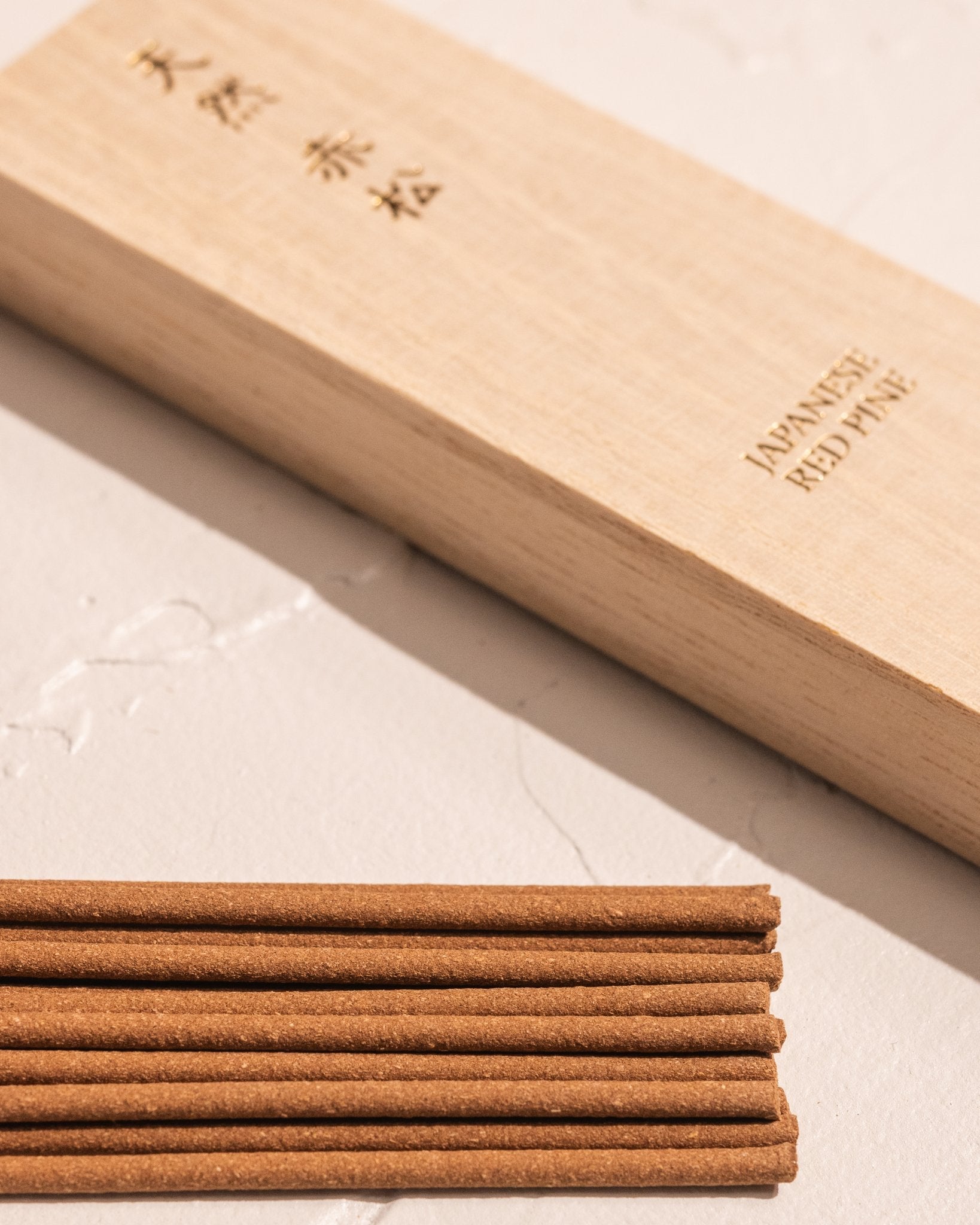 Close-up of Kousaido Japanese Red Pine incense sticks beside gold foil printed wood box