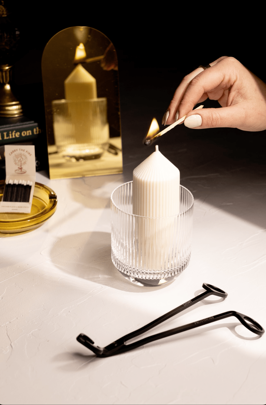Person lighting a white refill candle in a Light Provisions glass tumbler with a dark background