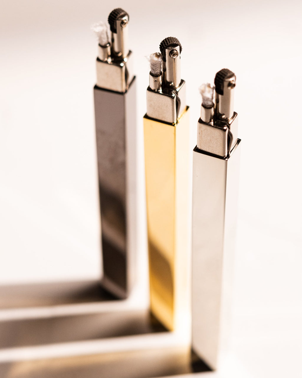Gold, silver, and black Tsubota Pearl Queue lighters standing upright with caps removed