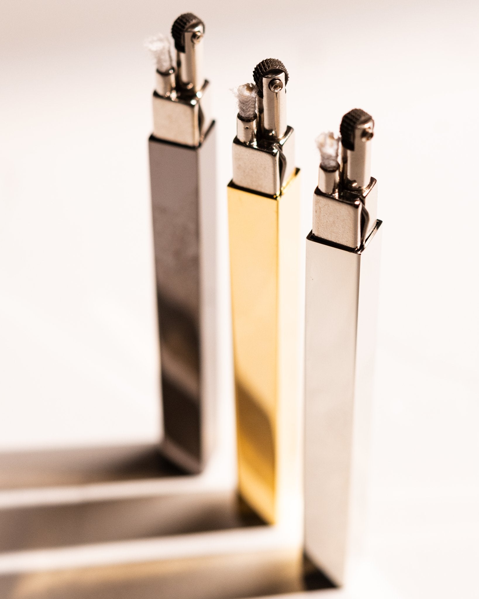 Gold, silver, and black Tsubota Pearl Queue lighters standing upright with caps removed