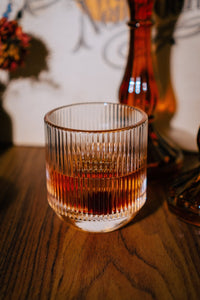 close up of glassware with a whiskey cocktail, the vibe is vintage orange and moody with a amber glass candle holder and a neil young record in the background