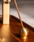 Close-up of sphere brass adjustable incense holder with incense stick, on teakwood tray with bolbo lighter in background