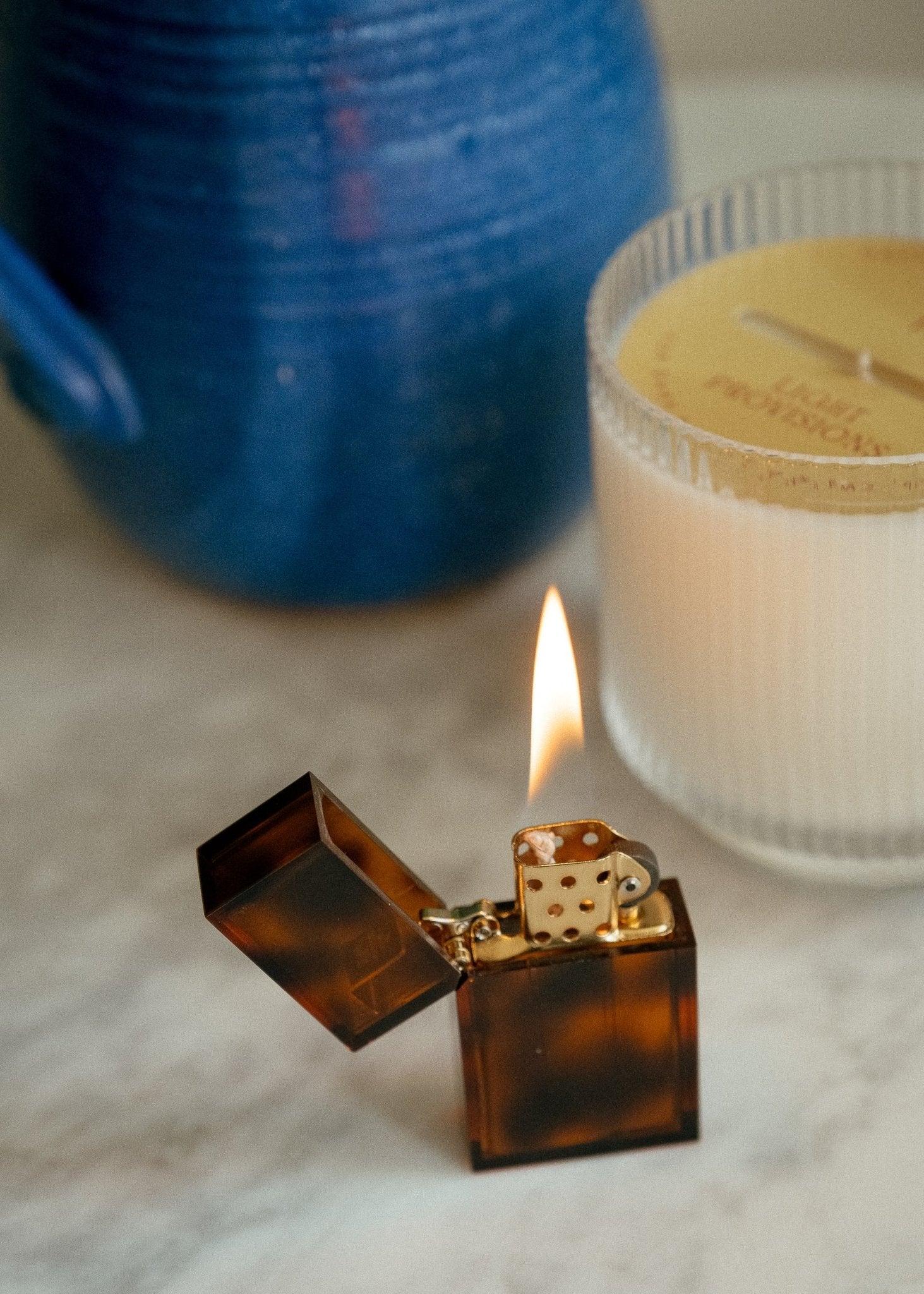 Translucent amber lighter by Tsubota Pearl, burning with soft flame next to ribbed glass Light Provisions candle