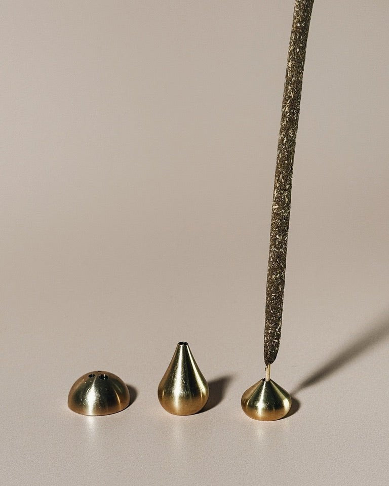 Medium brass waterdrop incense holders grouped together with incense sticks, photographed on a neutral surface.
