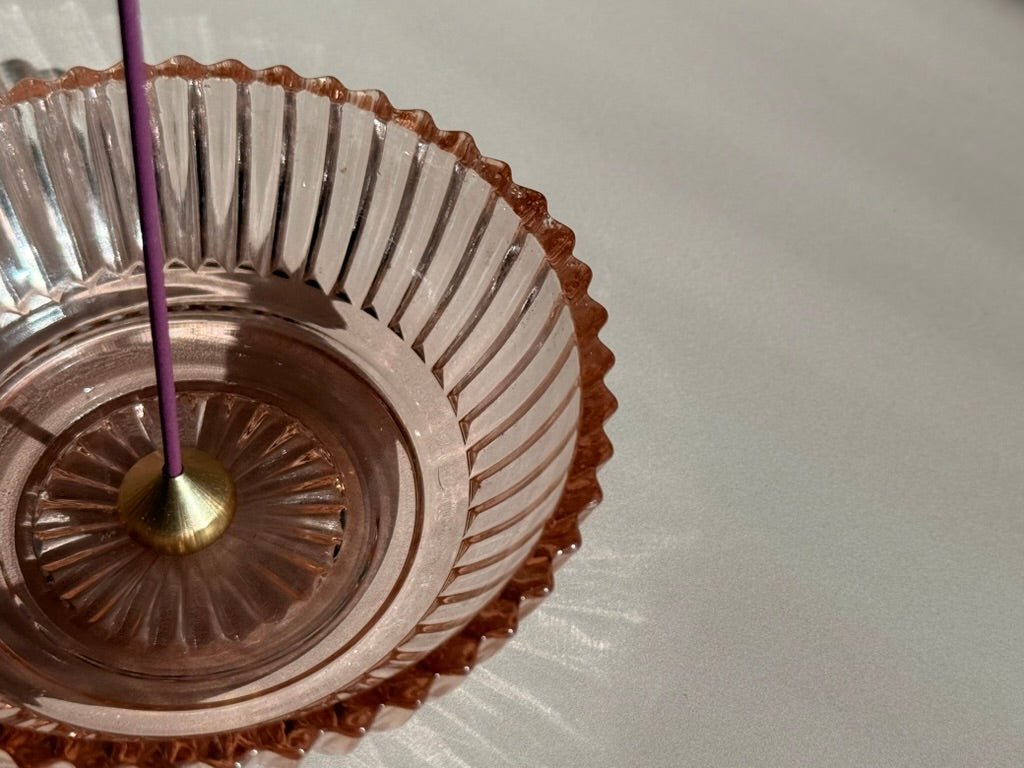 Medium brass waterdrop incense holder holding Japanese incense, photographed inside depression glass dish