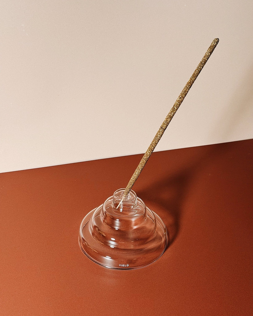 Incense stick in a clear glass stepped holder on a two-tone background