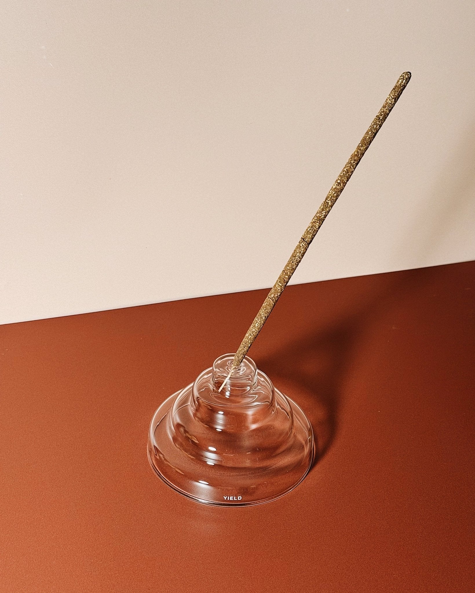 Incense stick in a clear glass stepped holder on a two-tone background