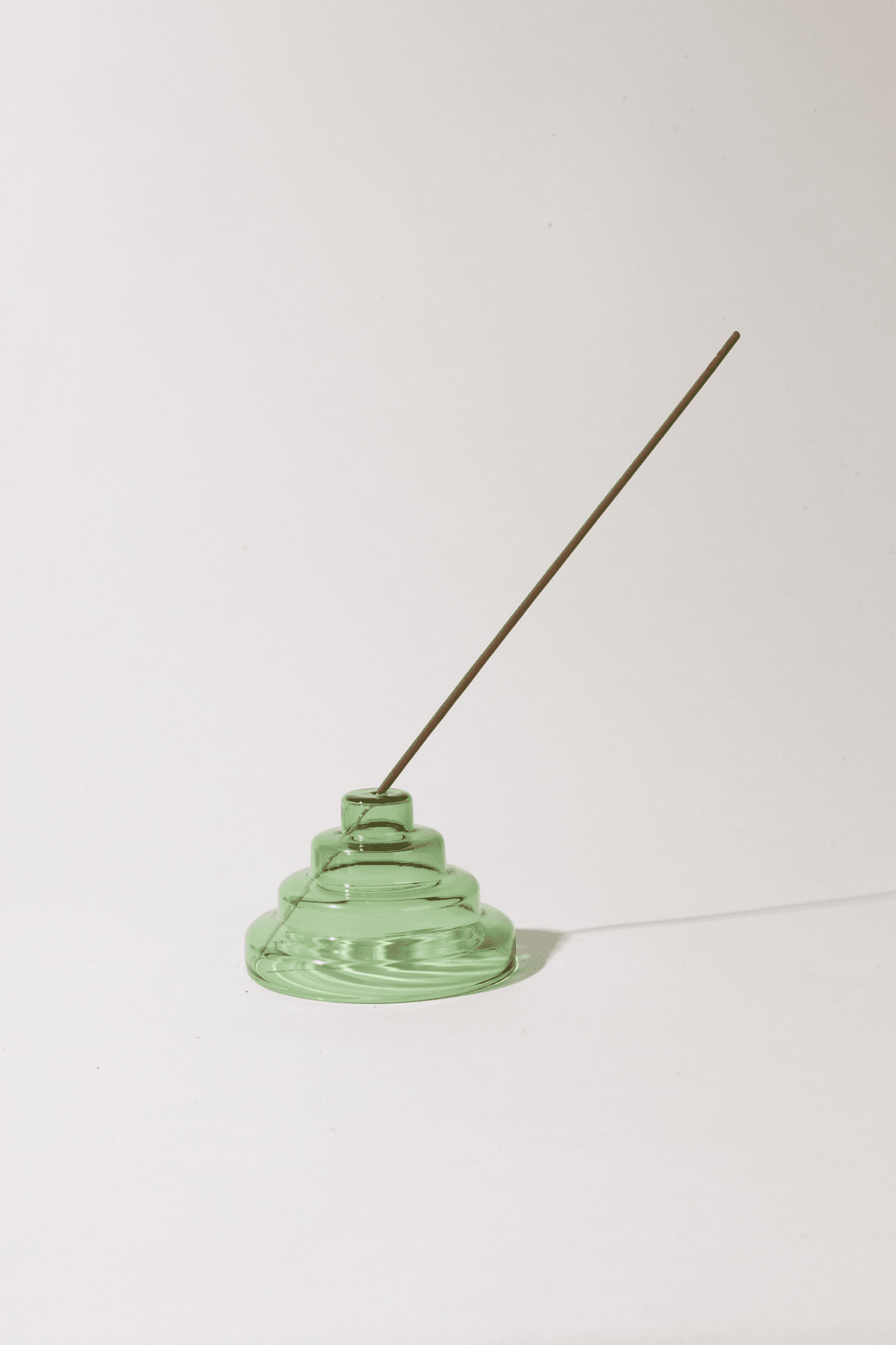 Green ceramic incense holder with a single incense stick on a white background