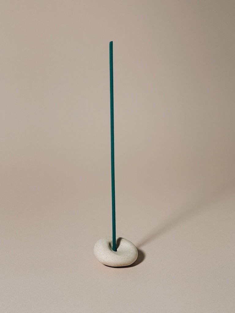 teal Incense stick on a beige pebble base against a beige background