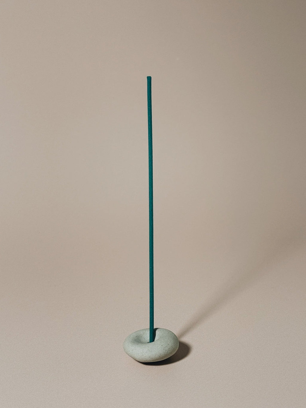 Teal incense stick in a gray pebble holder against a beige background