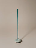 Teal incense stick in a gray pebble holder against a beige background