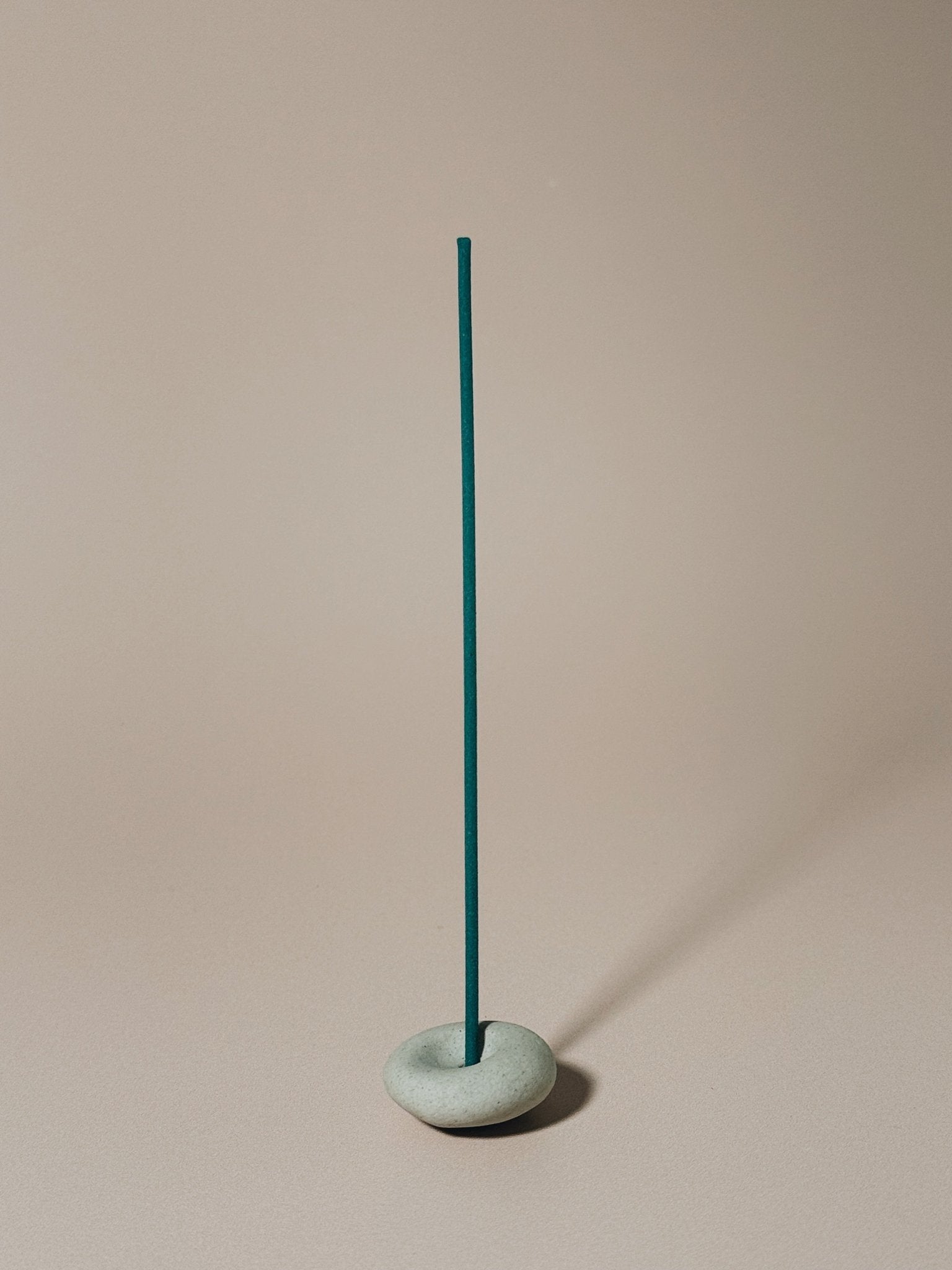 Teal incense stick in a gray pebble holder against a beige background
