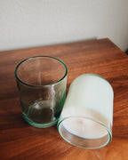 Two glass recycled aqua candle holders on a wooden surface with a white background