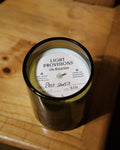 A dark amber glass jar candle with a white circular label reading 'LIGHT PROVISIONS On Rotation' and 'Palo Santo' written in script, placed on a wooden surface.