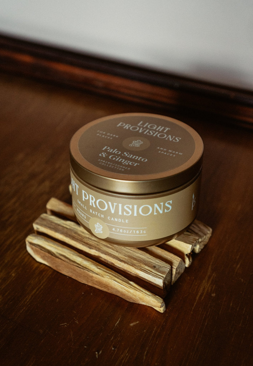 Palo Santo Ginger travel tin candle stacked with palo santo sticks on wooden surface