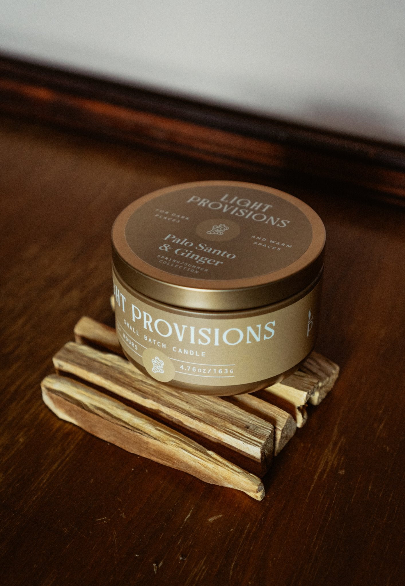 Palo Santo Ginger travel tin candle stacked with palo santo sticks on wooden surface