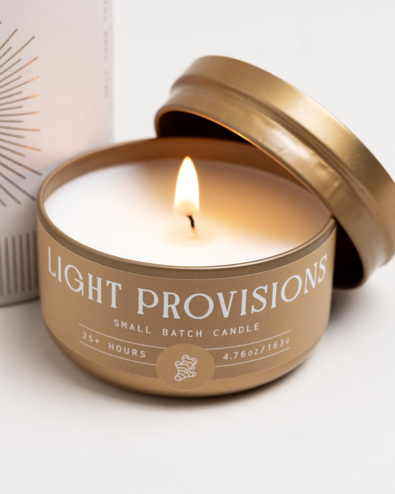 Close up of Palo Santo & Ginger travel tin candle burning, warm flame against white background.