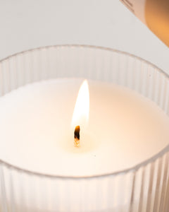 Macro of flame and melt pool in ribbed-glass tumbler for Palo Santo & Ginger, on white background.