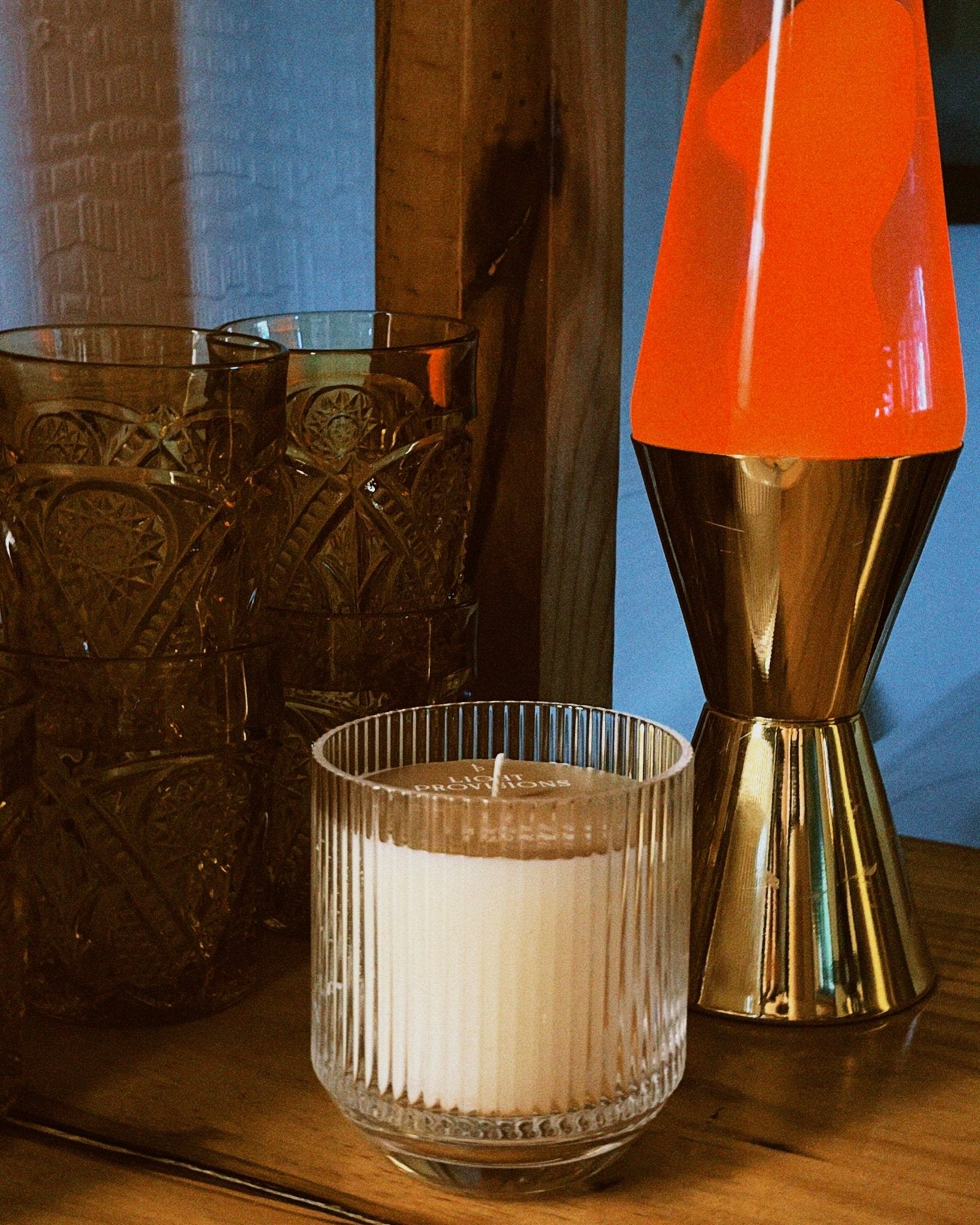 Candle in a glass holder next to a lava lamp with an orange top and gold base on a wooden surface.