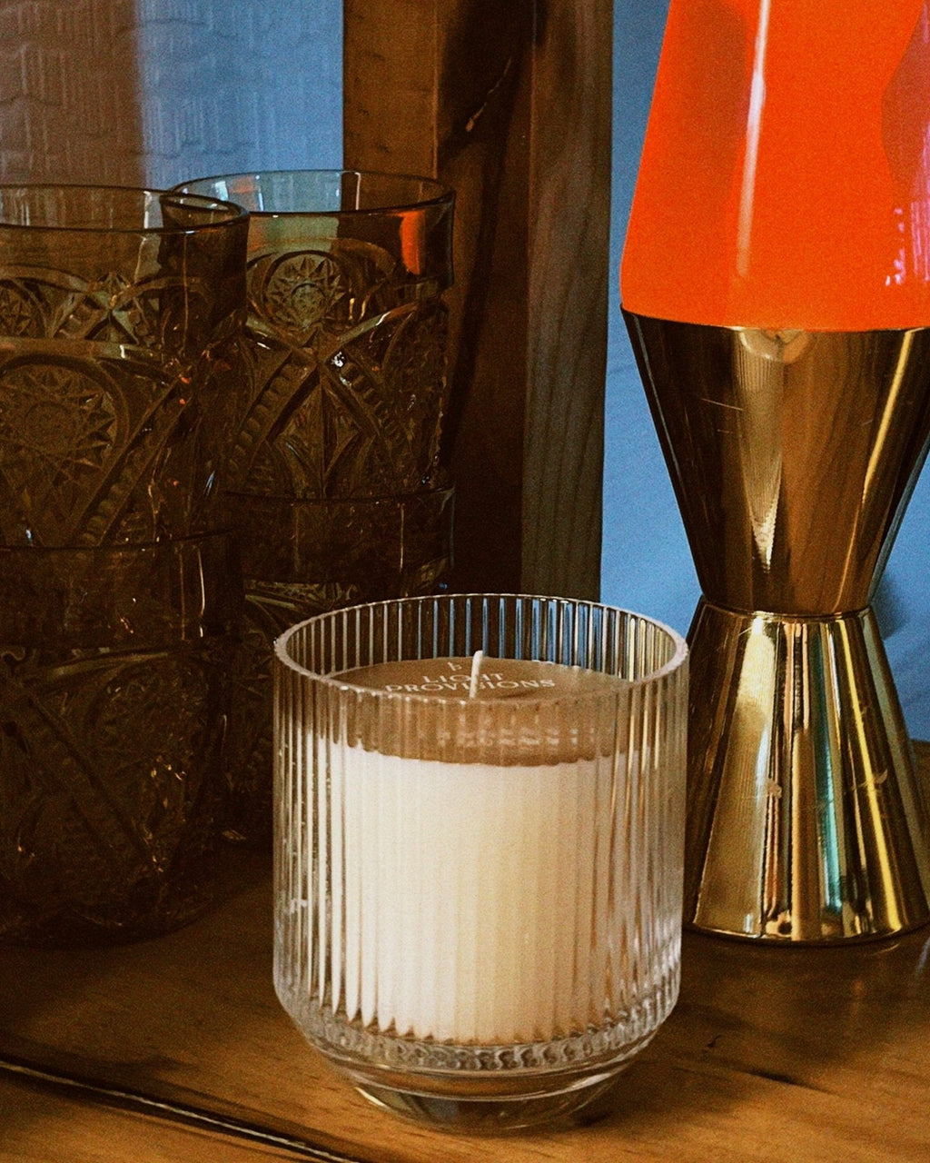 Candle in a glass holder next to a lava lamp with an orange top and gold base on a wooden surface, film style photo