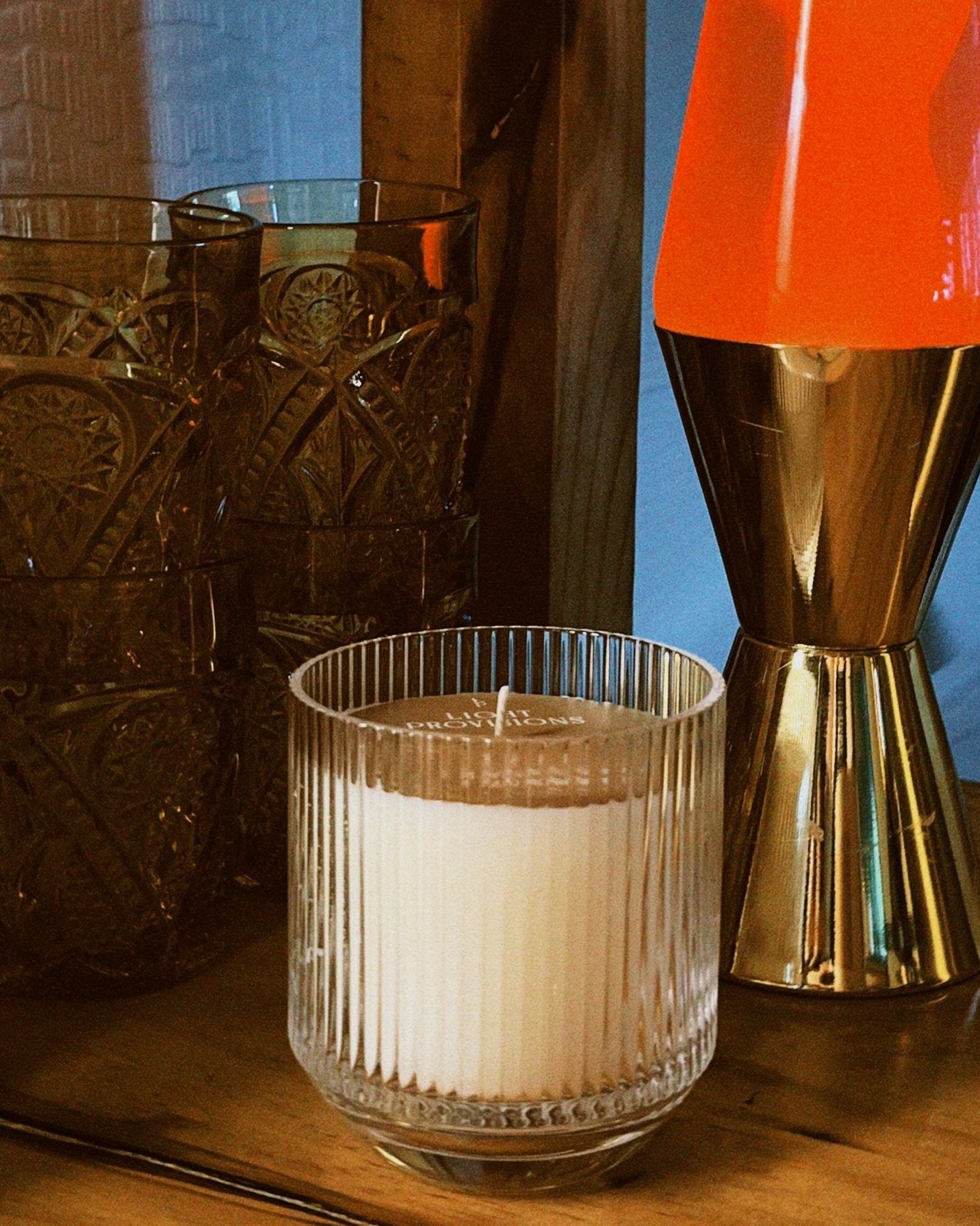 Candle in a glass holder next to a lava lamp with an orange top and gold base on a wooden surface, film style photo