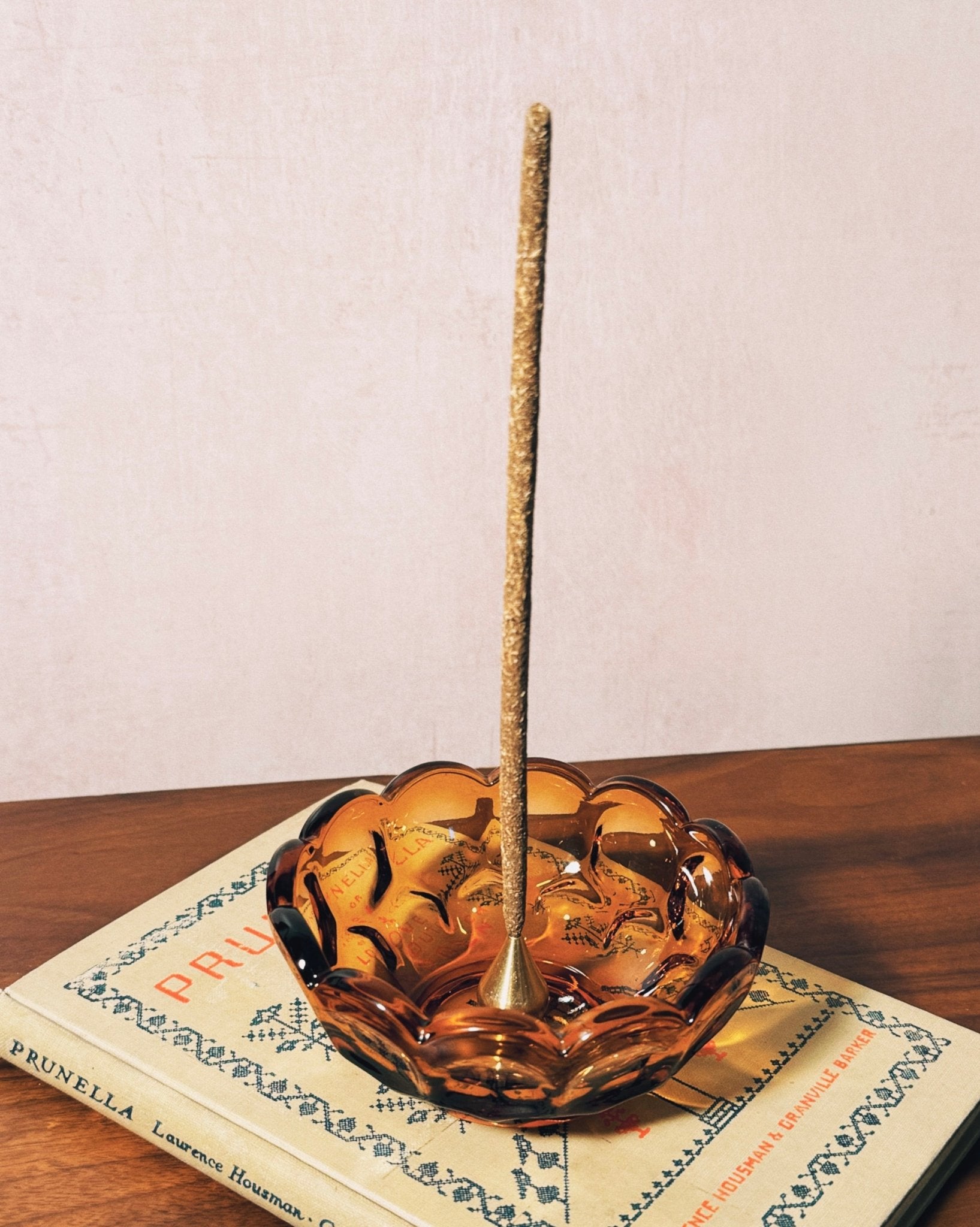 Palo Santo hand-rolled incense burning in a brass holder, inside a depression era vintage scalloped dish on a vintage book