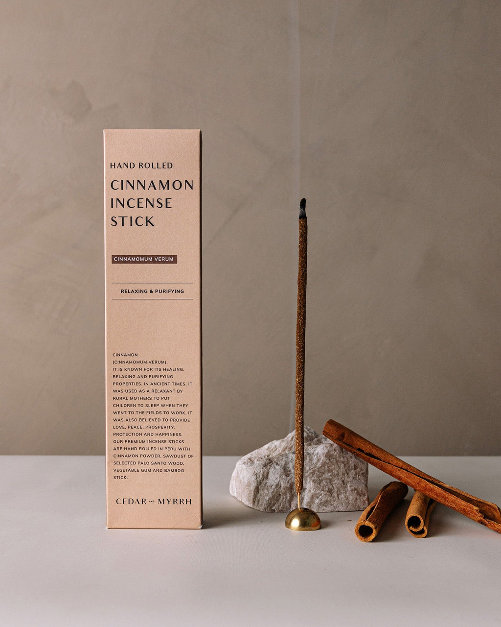 Hand-rolled cinnamon incense sticks displayed upright next to their minimalist packaging box on a neutral background
