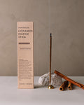 Hand-rolled cinnamon incense sticks displayed upright next to their minimalist packaging box on a neutral background