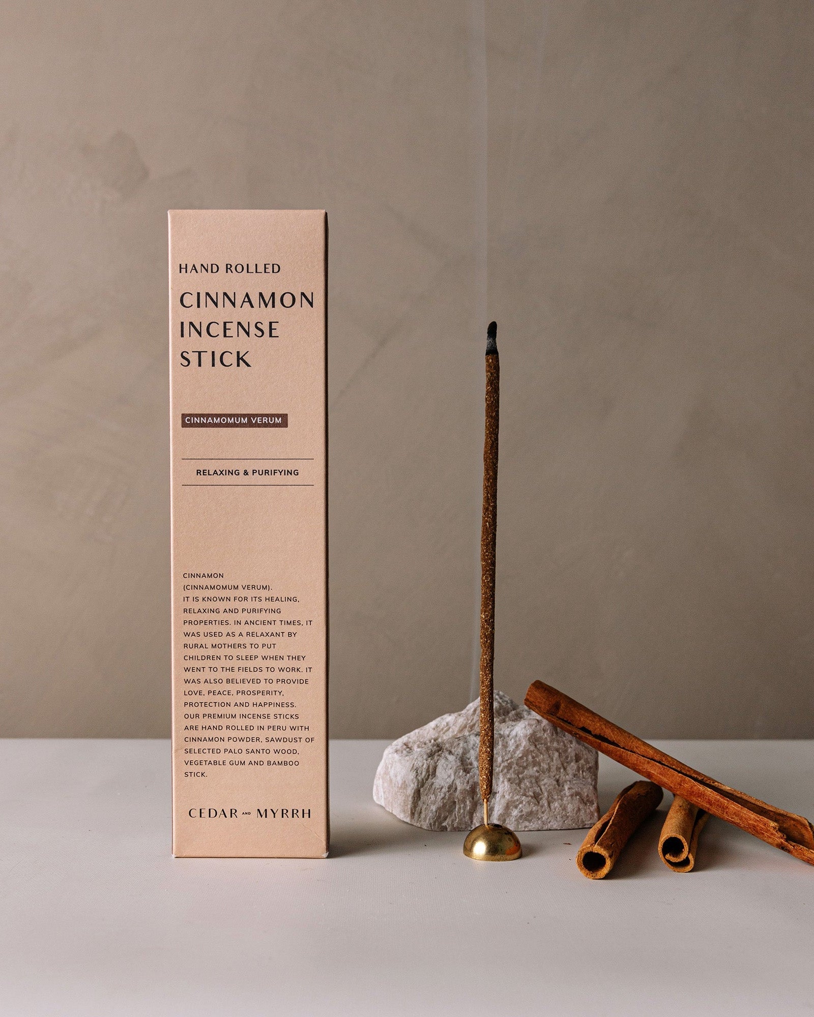 Hand-rolled cinnamon incense sticks displayed upright next to their minimalist packaging box on a neutral background