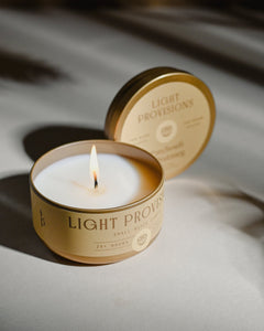 Light Provisions Patchouli & Nutmeg candle travel tin open with warm golden hour glow on soft neutral surface
