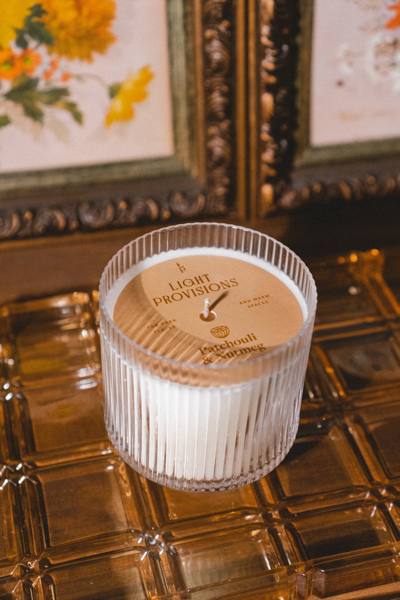 Patchouli & Nutmeg candle in signature glass tumbler with gold lid on vintage pressed glass amber tray and framed art