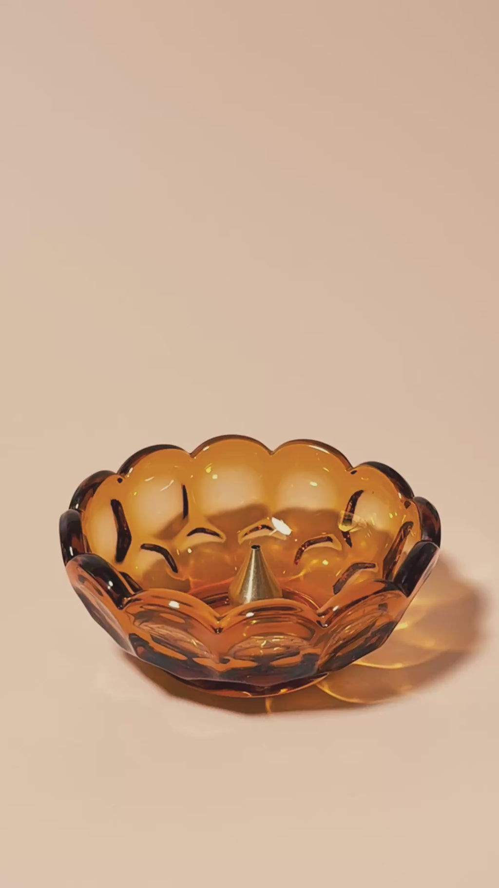 Hand placing incense into a brass holder inside a vintage amber scalloped glass dish.