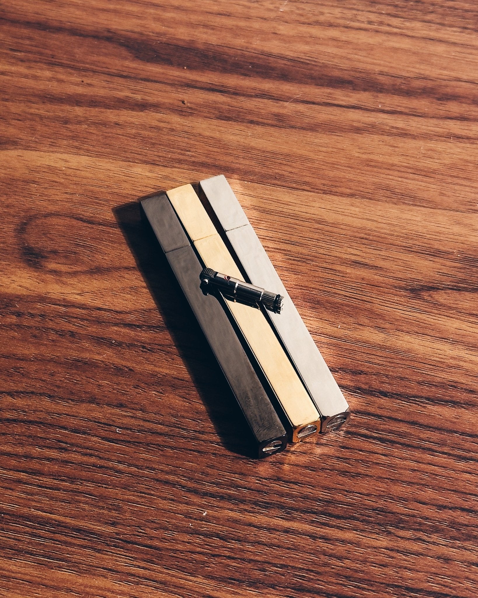 Three Tsubota Pearl Queue lighters in gold, silver, and black next to flint assembly replacement part