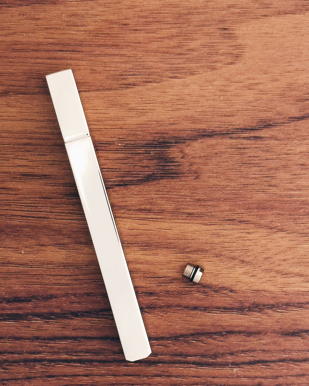 Tsubota Pearl lighter in silver finishes with a small metal threaded screw, arranged on a wooden surface.